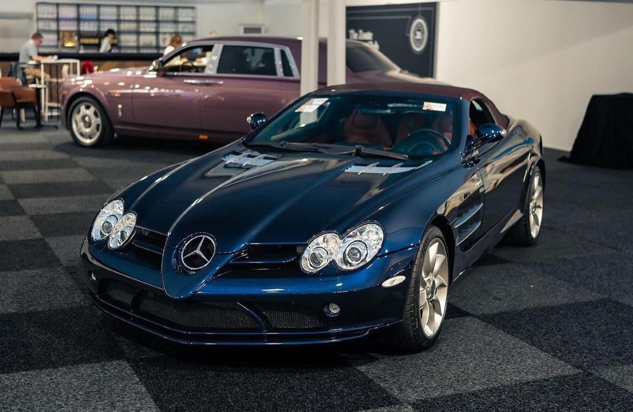 a front facing dark metallic blue Mercedes SLR McLaren with a pink Rolls Royce Phantom behind it